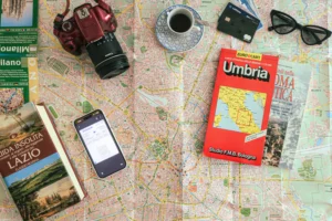 Photo à plat pour préparer un voyage en Italie : plan de Milan, carte routière de l'Ombrie, une carte d'embarquement, un appareil photo et des guides de voyage